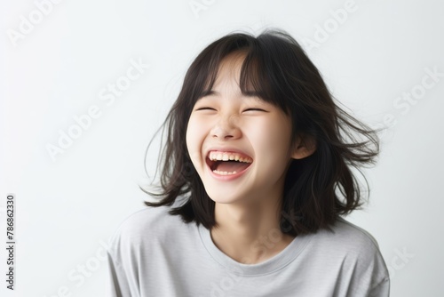 A beautiful Asian woman with long straight hair whose skin is tan is wearing an all white shirt, and smiling with a face which is full of happiness in a white room. Generative AI.