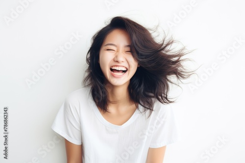 A beautiful Asian woman with long straight hair whose skin is tan is wearing an all white shirt, and smiling with a face which is full of happiness in a white room. Generative AI.