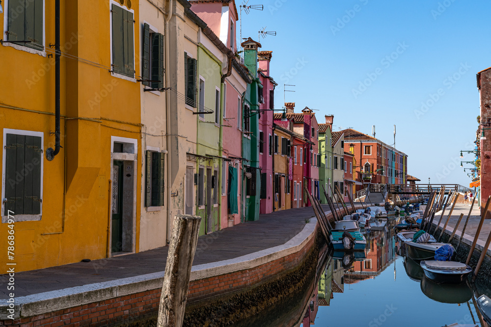 Blick auf die bunte Häuserfront in Burano (Italien), Boote schwimmen im Kanal, Häuser spiegeln sich im  Wasser