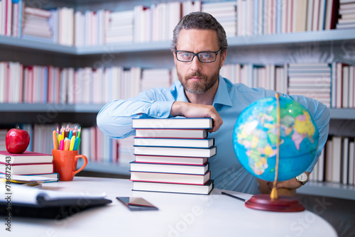 Portrait of teacher with book in library classroom. Handsome teacher in university library. Teachers Day. Teacher giving classes. School teacher in library. Tutor at college library on bookshelf.