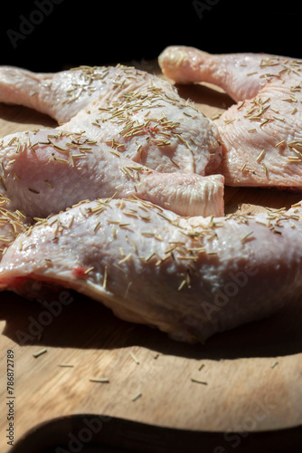 Raw free range organic chicken breasts covered with rosemary on a wooden chopping board