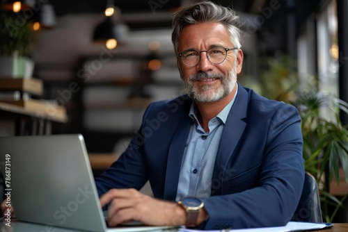 Smiling mature adult business man executive sitting at desk using laptop. Happy busy professional mid aged businessman ceo manager working on computer corporate technology in office