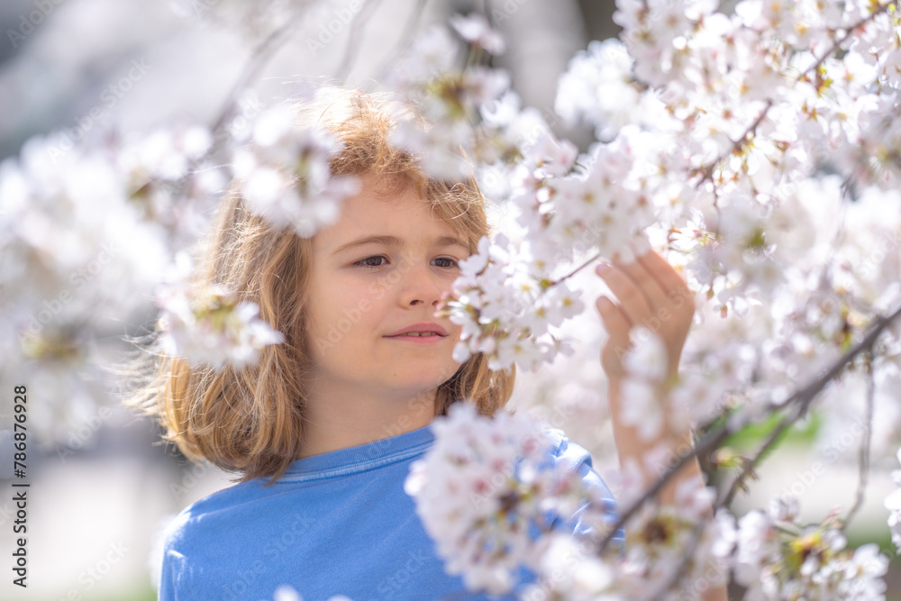 Happy spring. Close up portrait of smiling child face near white cherry blossom tree, spring flowers. Kid among branches of spring tree in blossoms. Cute kids face surrounded spring blossom flowers.