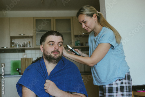 Wife gives her husband a funny haircut with a trimmer.
