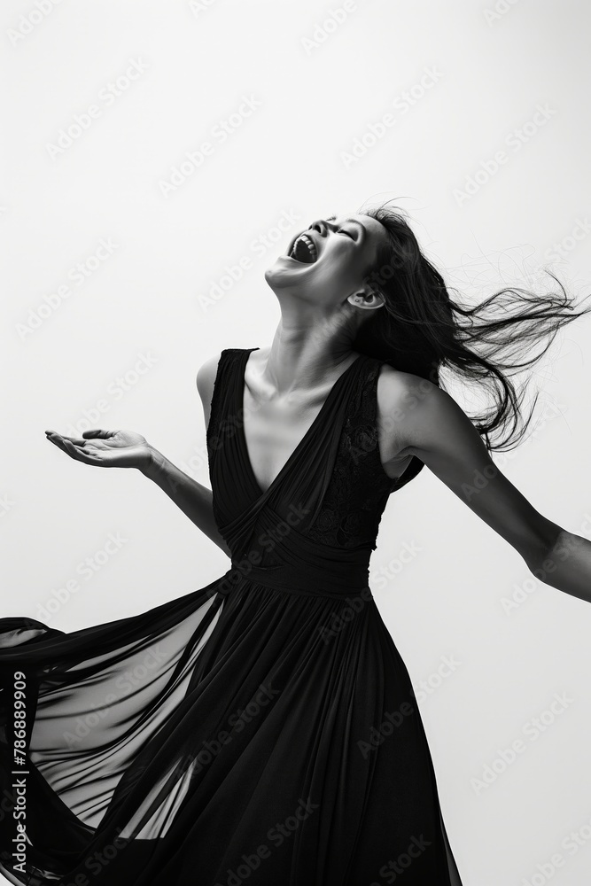 A monochrome image of a woman in a black dress laughing with her hair flowing, expressing carefree happiness.