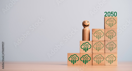 Miniature figure smile and standing on carbon reduction icon on wooden block cube for progressive of carbon credit footprint for carbon dioxide absorption to limit global warming within 2050 concept.