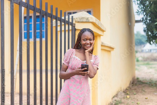 Young Black Woman Holding Phone beside Yellow School Building