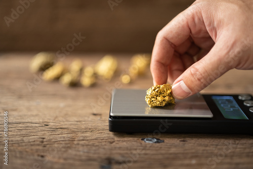 man's hand is holding a piece of pure gold mined from the mine and placing it on the weigher photo