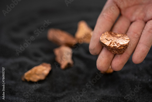 Man's hand holding a piece of copper to examine it for industrial use on black background
