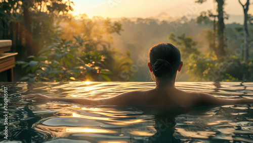 A woman relaxing in an infinity pool enjoying the natural scenery of lush greenery and trees at sunset, feeling calm after her spa experience © Kien