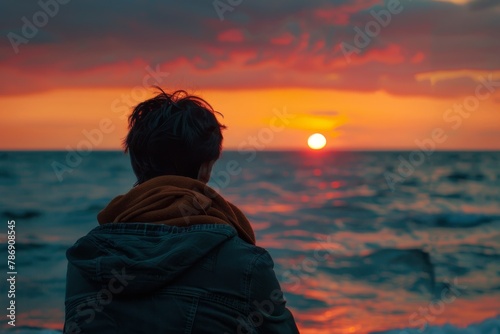 A lone figure sits on the sandy beach, facing the horizon as the sun dips below, casting a warm glow