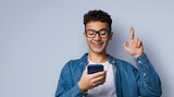 Smiling funny young man wear braces eye glasses hold typing text look read cell phone cellular smartphone cellphone, crossing fingers, praying hoping for good luck, isolated grey gray background.