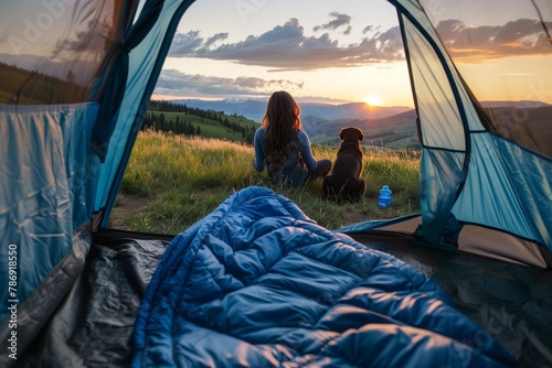 Young woman sitting in a tent with a sleeping bag and dog watching the view of a valley at sunset. Vibrant color photography. Wide angle lens. Beautiful The photo was taken from behind the girl's head photo