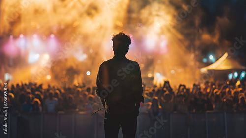  a performer, music artist in front of crowd on a huge stage, at a summer music festival