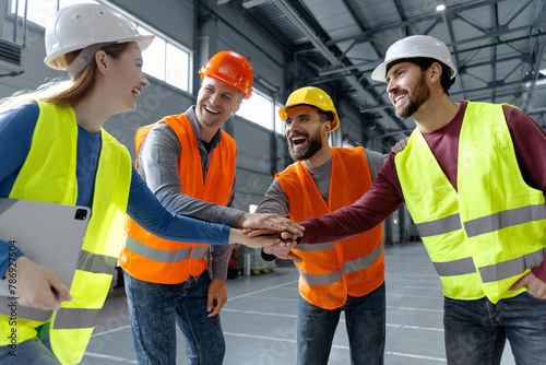 Successful team, managers, engineers wearing hard hats, work wear and vests holding hands together photo