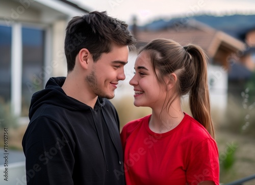 Portrait of a happy young couple in love, looking at each other and smiling while standing against a wooden house background. © Svetlana