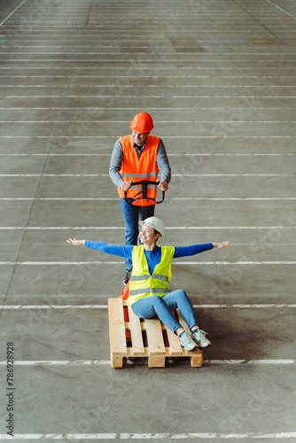 Top view, factory worker, engineer driving his colleague on pallet truck, fooling around, having fun