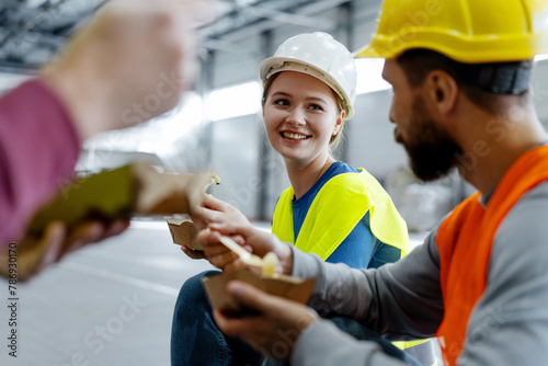 Happy smiling workers, construction wearing hard hats, vests sitting together, eating lunch, talking