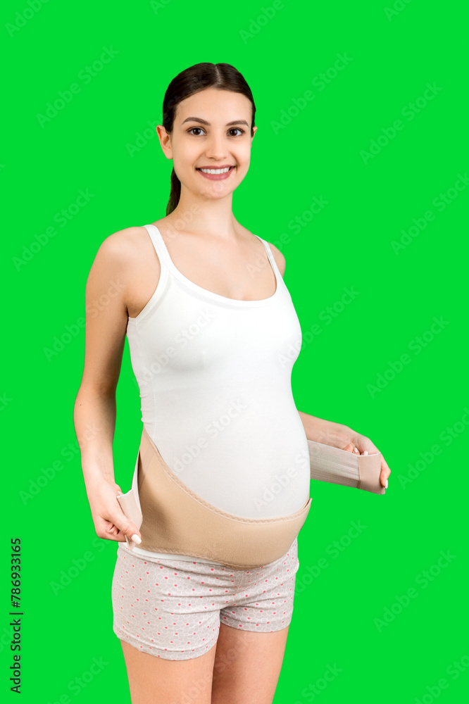 Portrait of pregnant woman putting on supporting bandage for reducing backache at green background with copy space. Orthopedic abdominal support belt concept Portrait of pregnant woman putting on supporting bandage for reducing backache at green background with copy space. Orthopedic abdominal support belt concept