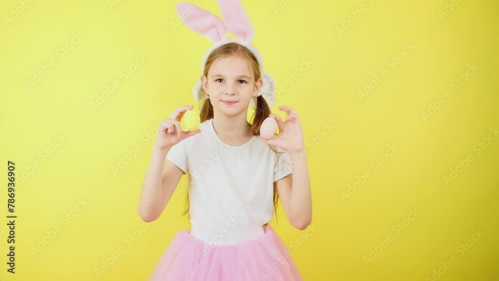 Cute little girl kid wears pink hare ears, holds colored easter eggs grow isolated over yellow background. Look at this decorated Easter eggs! Cute little girl kid wears pink hare ears, holds colored easter eggs grow isolated over yellow background. Look at this decorated Easter eggs!