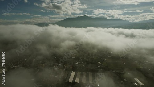 Aerial view of the town of Machachi hidden under thick clouds and fog, the dark mountain of Pasochoa volcano in the distance. Pichicnha province, Ecuador