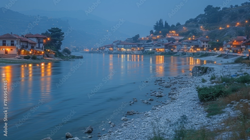 Obraz premium Evening settles over the ancient city of Berat, Albania, beautifully illuminated along the riverbank. This scenic view captures traditional architecture and calm waters with a touch of mystique.
