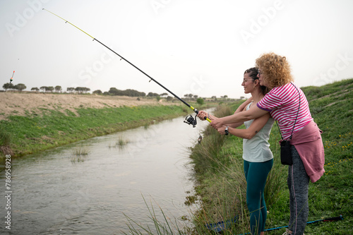 Mother and daughter learning fishing by a river while camping