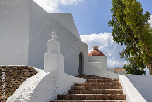 The picturesque steps leading to the iconic Puig de Missa church in Ibiza, Spain, are highlighted by the stark white walls and terracotta dome, offering a tranquil setting amidst natural beauty photo