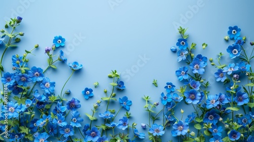 Vibrant green leaves and small blue forget-me-nots placed along one side of a pale grey surface, creating a fresh spring feel with significant negative space.