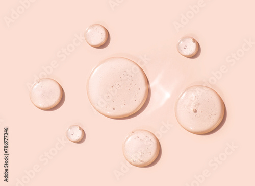 round drops of transparent gel serum on beige background