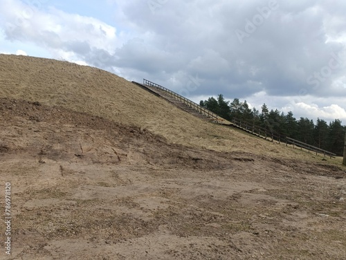 Salduve hill during cloudy day. Small hill. Grass is growing on hill. Staircase leading to the top. Cloudy day with white and gray clouds in sky. Nature. Salduves piliakalnis.