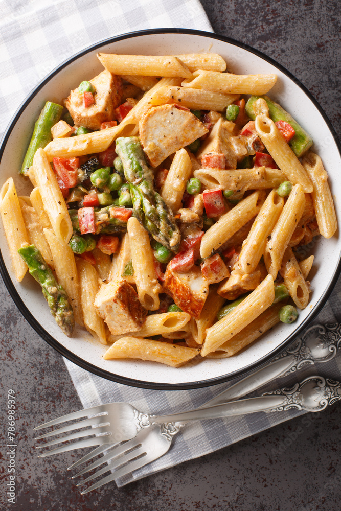 Penne pasta with chicken, asparagus, bell peppers and green peas in a creamy chipotle cheese sauce closeup in the bowl on the table. Vertical top view from above Penne pasta with chicken, asparagus, bell peppers and green peas in a creamy chipotle cheese sauce closeup in the bowl on the table. Vertical top view from above