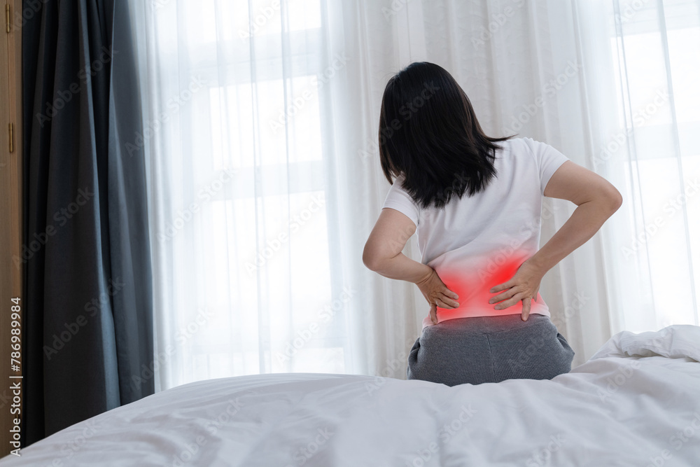 Women with lower back pain sitting by the bed Women with lower back pain sitting by the bed