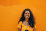 A vibrant Indian woman, in her late 20s, smiles warmly while recommending a smartphone app on a vibrant orange background, demonstrating her tech-savvy nature and infectious energy.