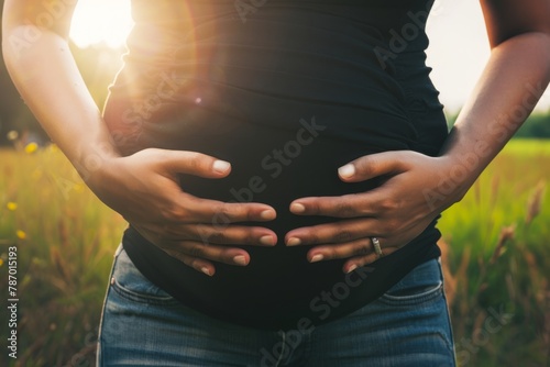 Pregnant woman lovingly holding her belly while standing in a sunny field. photo