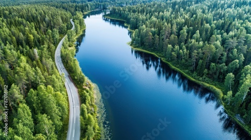 Aerial view of road between green summer forest and blue lake in Finland Lapland
