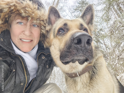 Adult girl with shepherd dog taking selfies in a winter forest. Middle aged woman and big shepherd dog on nature in cold day. Friendship, love, communication, fun, hugs
