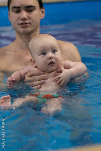 Portrait of the curious baby with a swim coach in a swimming pool. Swimming lessons for newborns. Closeup.