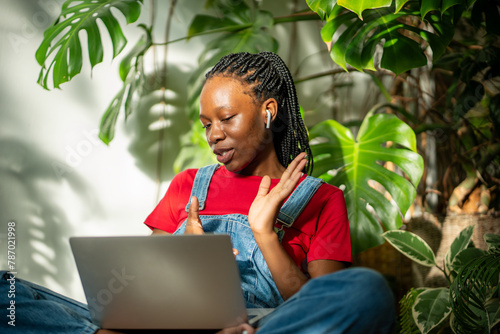 Focused african american woman with laptop sitting in urban jungle interior wearing earphones make video call. Interested black young female talking on online conference enthusiastically gesturing.