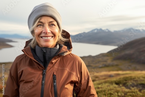 Portrait of a grinning woman in her 50s donning a durable down jacket on panoramic mountain vista