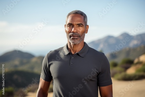Portrait of a glad afro-american man in his 50s donning a classy polo shirt isolated in panoramic mountain vista photo