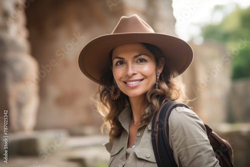 Portrait of a smiling woman in her 40s wearing a rugged cowboy hat isolated on backdrop of ancient ruins