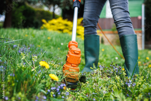 Gardener trimming grass at backyard. Electric grass trimmer. Lawn care by gardening equipment photo