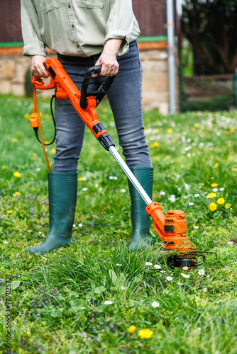 String trimmer. Woman is trimming grass in garden. Lawn care in spring