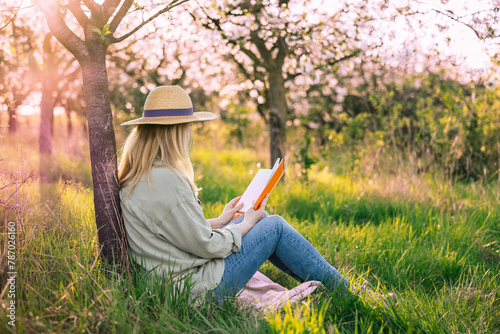 Relaxed woman sitting under blooming cherry tree and reading book to improve her mindfulness. Enjoying moments of solitude and relaxation in spring orchard © encierro