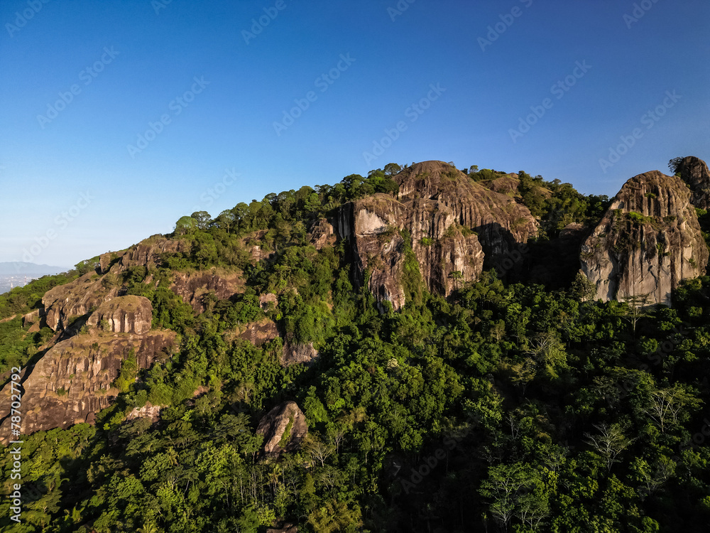 Aerial view of Nglanggeran Ancient Volcano in Gunungkidul, Yogyakarta, Indonesia with clear blue sky background. Rocky mountains with a lot of tree. Indonesian rainforest from above.