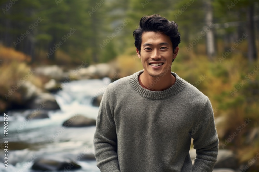 Portrait of a grinning asian man in his 20s dressed in a warm wool sweater on tranquil forest stream Portrait of a grinning asian man in his 20s dressed in a warm wool sweater on tranquil forest stream