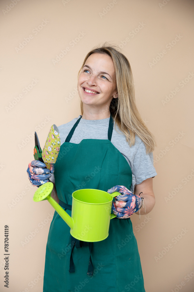 female gardener, early 40s, with floral gloves, green watering can posing in front of brown background female gardener, early 40s, with floral gloves, green watering can posing in front of brown background