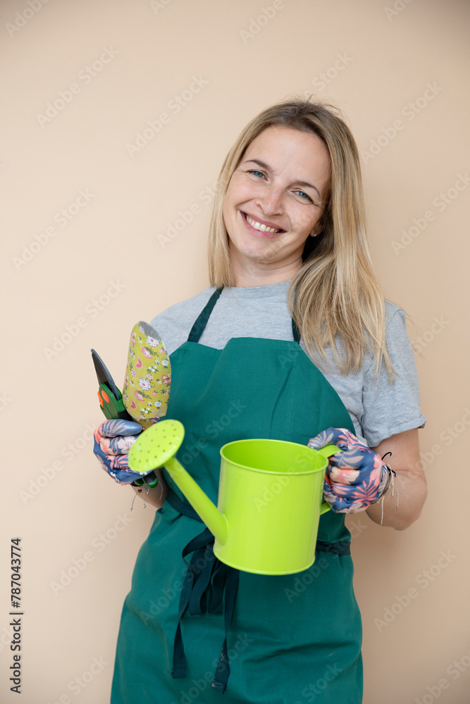 female gardener, early 40s, with floral gloves, green watering can posing in front of brown background female gardener, early 40s, with floral gloves, green watering can posing in front of brown background