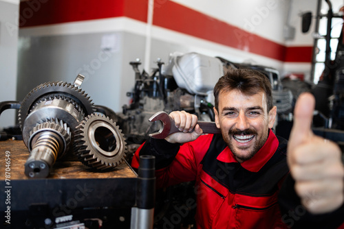 Portrait of smiling serviceman repairing transmission inside workshop.